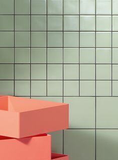 two pink boxes sitting on top of each other in front of a tiled bathroom wall