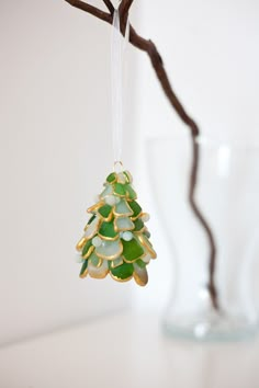 a christmas tree ornament hanging from a twig on a branch in front of a glass vase