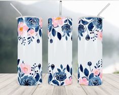 three white and blue floral tumblers with straws on a wooden table in front of a lake