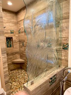 a glass shower door in a bathroom with pebbles on the floor and palm leaf designs