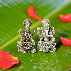 two small silver statues sitting on top of a green leaf next to red flower petals