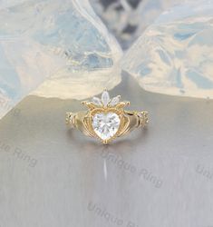 The Irish Crown Heart ring is a beautiful and unique ring that is perfect for engagements or as a statement piece. The ring features a Claddagh design with an exaggerated gemstone in the center. The hand holding the heart is a symbol of love and friendship and the crown atop the heart represents loyalty. This ring is truly a work of art and would make an amazing engagement ring or addition to any jewelry collection. Claddagh Ring, Heart Shape Colorless Moissanite Claddagh Ring, Celtic Knot Ring, Irish Claddagh Engagement Ring, Claddagh Ring With Diamond, Claughdaugh Engagement Ring, Engagement Rings Claddagh, Unique Claddagh Ring, Claddagh Ring Engagement, Irish Claddagh Rings, Irish Wedding Ring, Gold Hand Ring