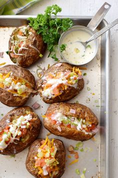 several baked potatoes with toppings on a tray next to a bowl of ranch dressing