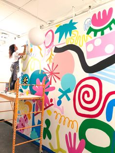 a man on a scaffolding ladder painting a mural with colorful shapes and colors