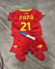 a red and yellow soccer uniform laying on top of a bed next to a pair of shoes