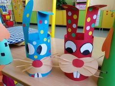 three colorful paper cups with faces on them sitting on top of a wooden table in a classroom