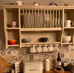 a kitchen counter with dishes and cups on it, next to a wooden shelf filled with plates