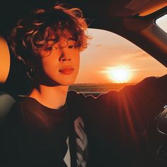 a woman sitting in the driver's seat of a car as the sun sets