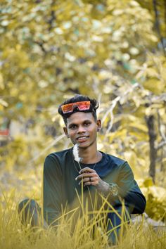 a man sitting in the middle of tall grass with his hair styled up and sunglasses on