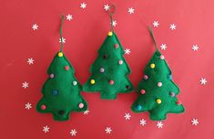 three felt christmas trees hanging from strings on a red background