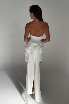 the back of a woman in a white dress with a large bow on it's waist