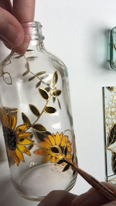 a person is holding a paintbrush and painting a glass jar with flowers on it