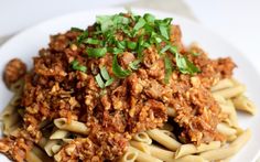 a white plate topped with pasta and meat covered in sauce on top of green garnish