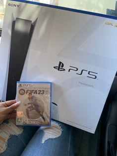 a person holding up a video game in front of a playstation ps5 console box