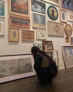 a person sitting on the floor in front of a wall covered with pictures and framed art