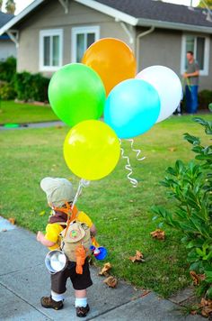 a little boy holding some balloons in front of a house on the side of the road