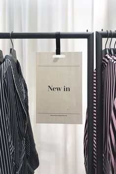 two shirts hanging on clothes racks in front of a window with the words new in