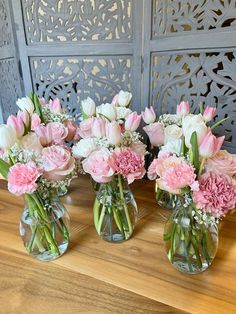 three vases filled with pink and white flowers sitting on a wooden table next to a wall