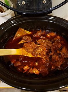 a wooden spoon in a slow cooker filled with meat