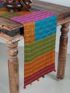 a multicolored table runner on top of a wooden table next to a bowl of fruit