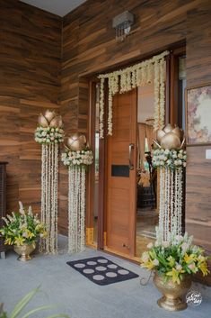 the entrance to a house decorated with white flowers and gold vases filled with greenery