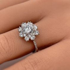 a woman's hand with a diamond ring on her left hand and the center stone is surrounded by smaller diamonds