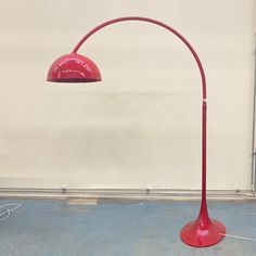 a red floor lamp sitting on top of a cement floor next to a white wall