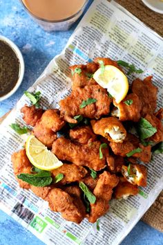 fried chicken with lemon slices and herbs on newspaper next to cup of tea