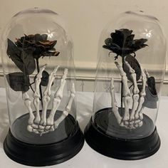 two glass domes with skeleton hands and flowers in them sitting on a white counter top