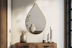 a mirror hanging on the wall next to a dresser with vases and other items