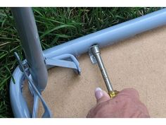 a person holding a metal object in their hand next to a blue bike frame on the ground