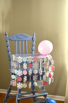 a blue rocking chair with snowflakes and balloons on it's back, in front of a beige wall