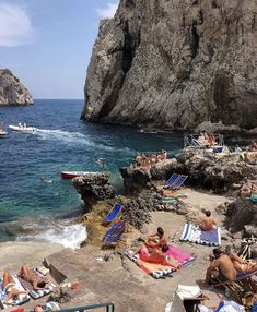 people are lounging on the rocks near the water and in the sun, while others swim