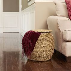 a basket sitting on the floor in front of a white couch with red throw pillows