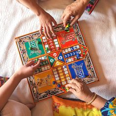 two people playing a board game on a bed with white sheets and colorful cloths