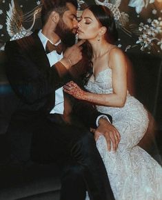 a man and woman sitting next to each other in front of a wall with flowers