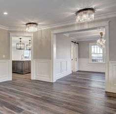 an empty living room with wood floors and chandelier hanging from the ceiling in front of two windows