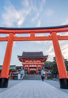 an orange and black gate with people walking underneath it in front of a building that looks like a temple