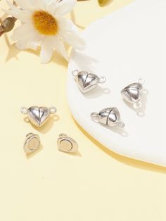 three pieces of silver jewelry sitting on top of a white table next to a flower