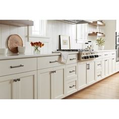 a large kitchen with white cabinets and wood floors is pictured in this image, there are flowers on the counter