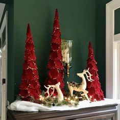 christmas decorations on top of a dresser with red trees and white deer figurines