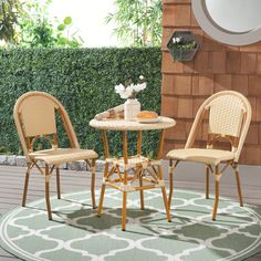 two chairs and a table on a rug in front of a wall with green plants