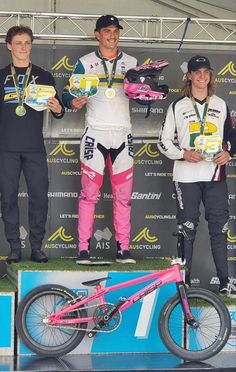 three men standing on top of a podium holding up their medals and bicycles in front of them