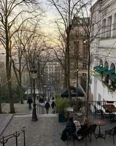 people are sitting at tables in the middle of an alleyway with trees and buildings