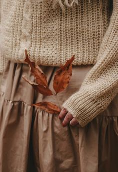 a close up of a person wearing a sweater and skirt with leaves on the bottom