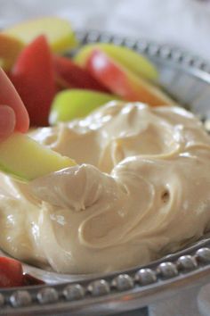 a person dipping some fruit into a bowl with cream cheese on the top and apples in the background