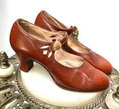 "New Old Stock & Never Worn, Late 1920's-Early 1930's \"Enna Jettick\" Art Deco Cinnamon Brown Kid Leather Mary Janes. Single side button, cut-outs at sides, decorative enamel slide buckle w morning glory flowers. I purchased the Stock of a Shoe Store that closed in the 1950's, all of the stock was very early. Heel measures 2 1/4″ high. Narrow Size, Measured inside with a soft measuring tape pressed into the sole, heel to toe-9 1/4\", width at ball of foot inside-2 5/8″. Compare these measurements to the insides of your own shoes to assure fit as all sales are final. Outsole measures heel to toe 9 3/8\", width at ball of foot 2 3/4\". The Leather is in Outstanding Condition, No noteworthy drying or brittleness. The Straps are Still flexible, the Vamp of the Shoe is edged in fine brown Gros Vintage Closed Toe Heels With Penny Strap, Vintage Heels With Penny Strap And Almond Toe, Vintage Almond Toe Heels With Penny Strap, 40s Shoes, Vintage Brown Heels, Vintage Closed Toe Heels For Vintage Events, Vintage Closed Toe Heels For Galas, 1960s Shoes, 1930s Shoes