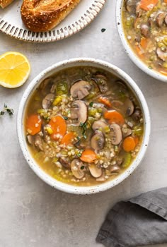 two bowls of mushroom soup on a table with bread and lemon wedges next to it