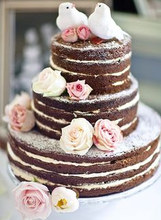 a three tiered cake with flowers on the side and two birds sitting on top