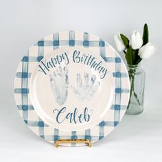 a blue and white plate with two handprints on it next to a vase filled with tulips